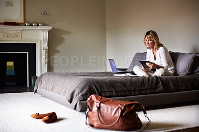 Buy stock photo Shot of a mature businesswoman sitting on a hotel bed using a laptop and digital tablet