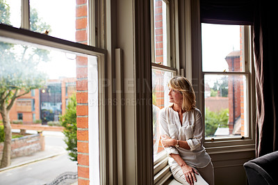 Buy stock photo Shot of an attractive mature woman looking through her living room window