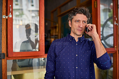 Buy stock photo Shot of a man talking on his cellphone wile standing in front of a cafe