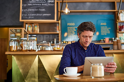 Buy stock photo Shot of a man working on a digital tablet in a cafe