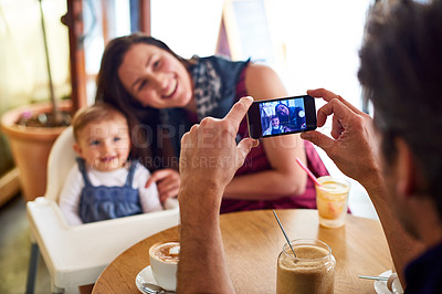 Buy stock photo Shot of a father taking a picture of his wife and baby girl while sitting in a cafe