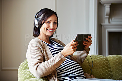 Buy stock photo Portrait of a pregnant woman sitting on her sofa listening to music on a digital tablet