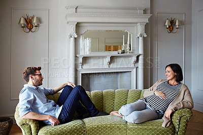 Buy stock photo Shot of a young pregnant woman talking with her husband on their sofa