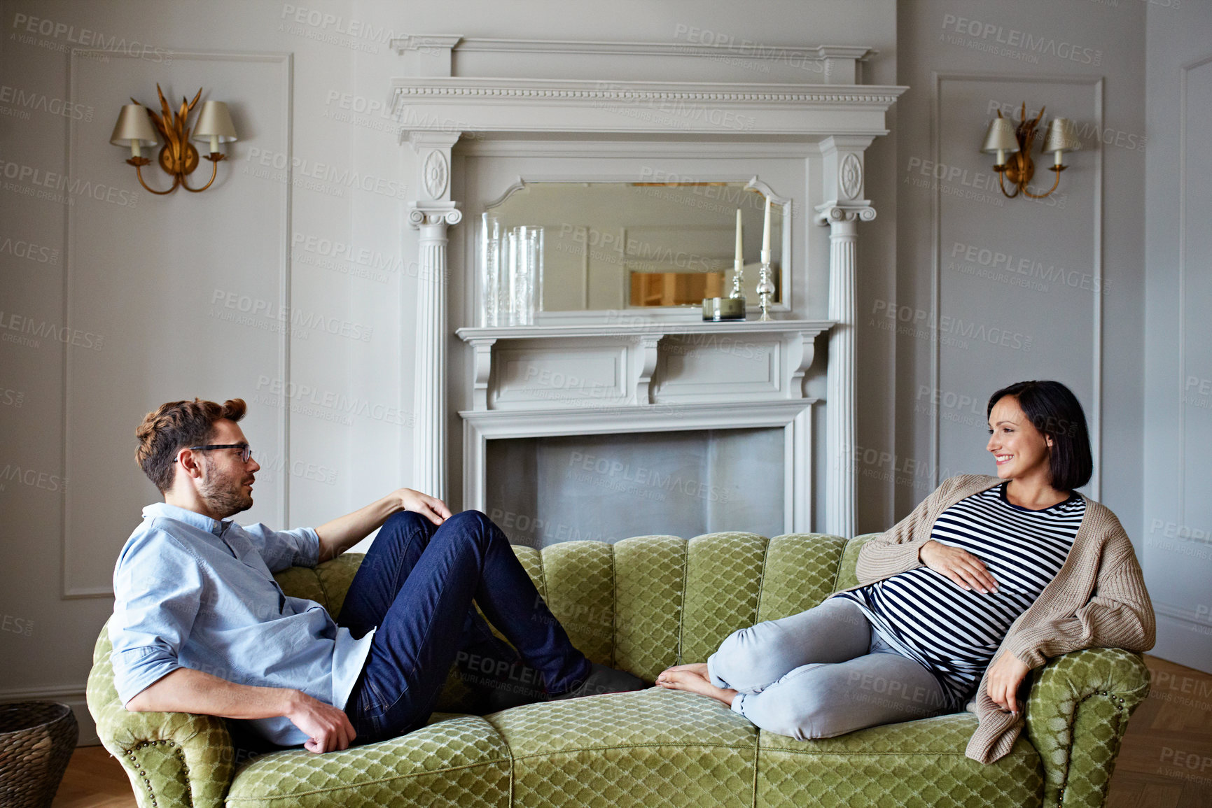 Buy stock photo Shot of a young pregnant woman talking with her husband on their sofa