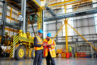 Buy stock photo Shot of two warehouse workers talking together over a digital tablet