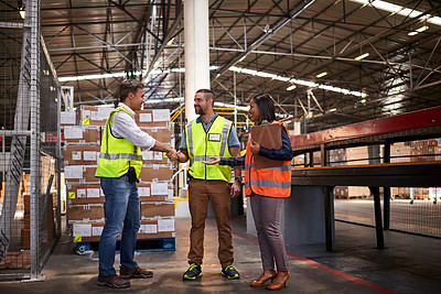 Buy stock photo Shot of two workers shaking hands together while standing in a large warehouse