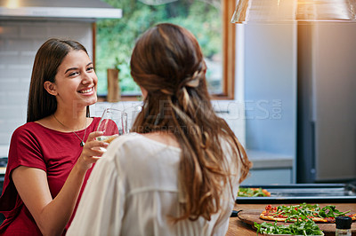 Buy stock photo Shot of two friends hanging out in a kitchen drinking wine together and eating pizza