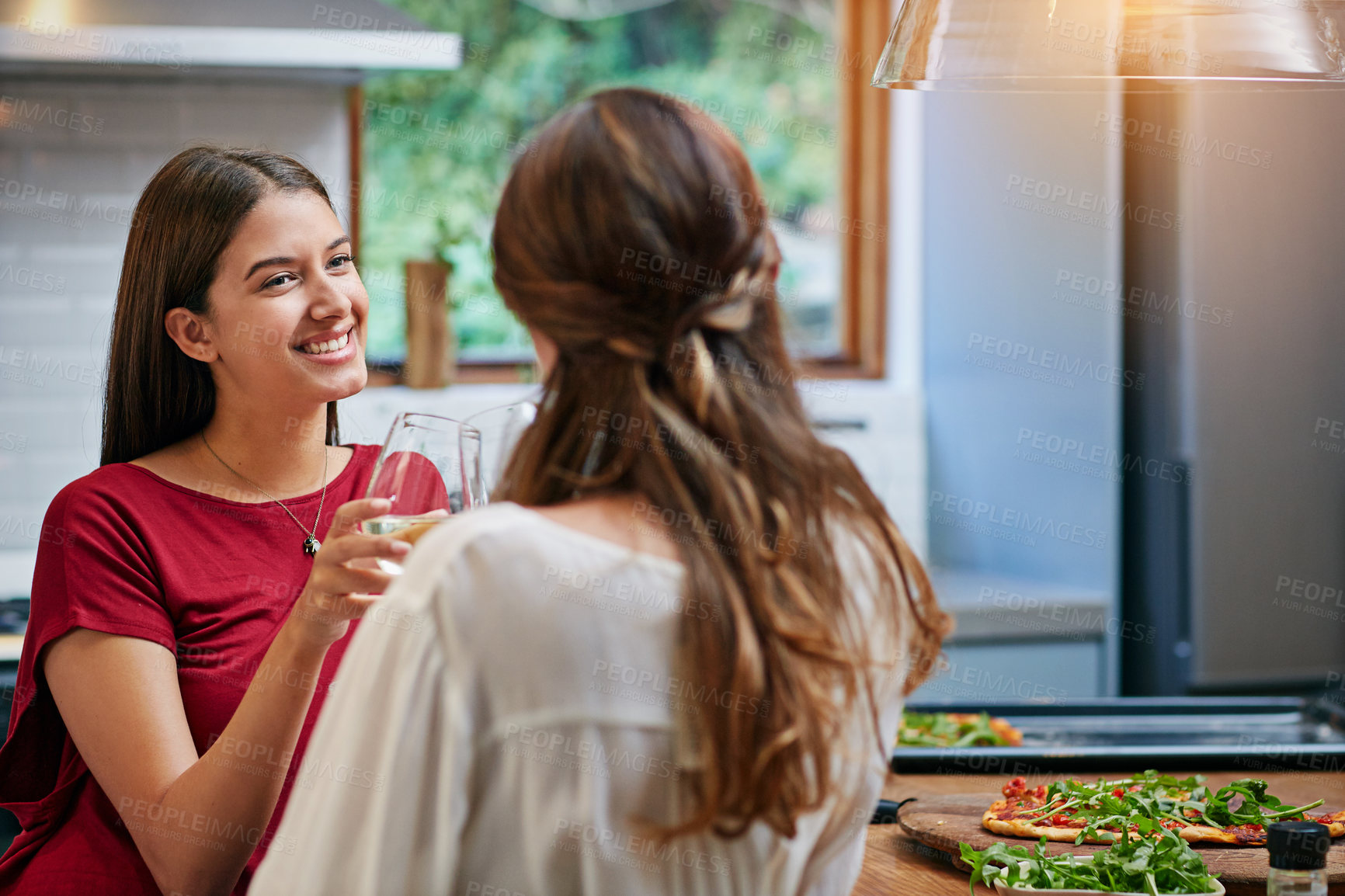 Buy stock photo Shot of two friends hanging out in a kitchen drinking wine together and eating pizza