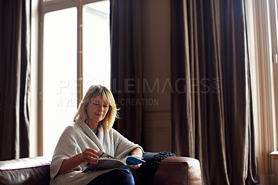 Buy stock photo Shot of a mature woman reading a book while sitting on her sofa