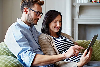 Buy stock photo Shot of a pregnant woman and her husband using a digital tablet while sitting on their sofa