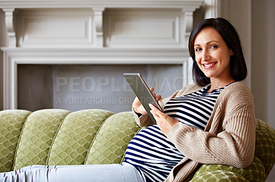 Buy stock photo Portrait of a pregnant woman sitting on her sofa and using a digital tablet