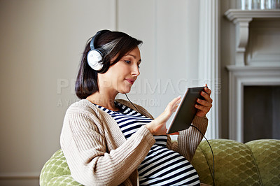 Buy stock photo Shot of a pregnant woman sitting on her sofa listening to music on a digital tablet