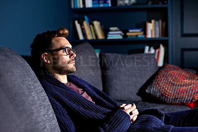 Buy stock photo Shot of a young man sitting on the sofa watching television in the evening