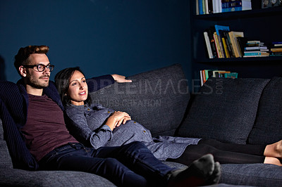 Buy stock photo Shot of a pregnant woman and her husband sitting on the sofa watching television in the evening
