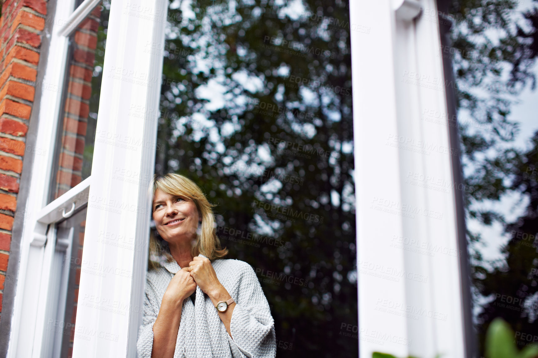 Buy stock photo Shot of a mature woman looking out of her living room window