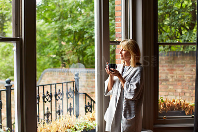 Buy stock photo Shot of a mature woman drinking tea while looking out of her living room window