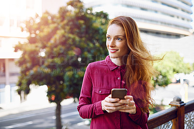 Buy stock photo Shot of a young woman sending a text message while standing outside