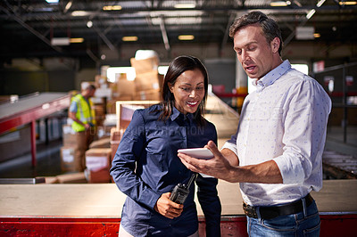 Buy stock photo Shot of two colleagues looking at a digital tablet while standing in a large warehouse