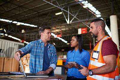 Buy stock photo Shot of a group of coworkers talking together over a laptop while standing in a large warehouse