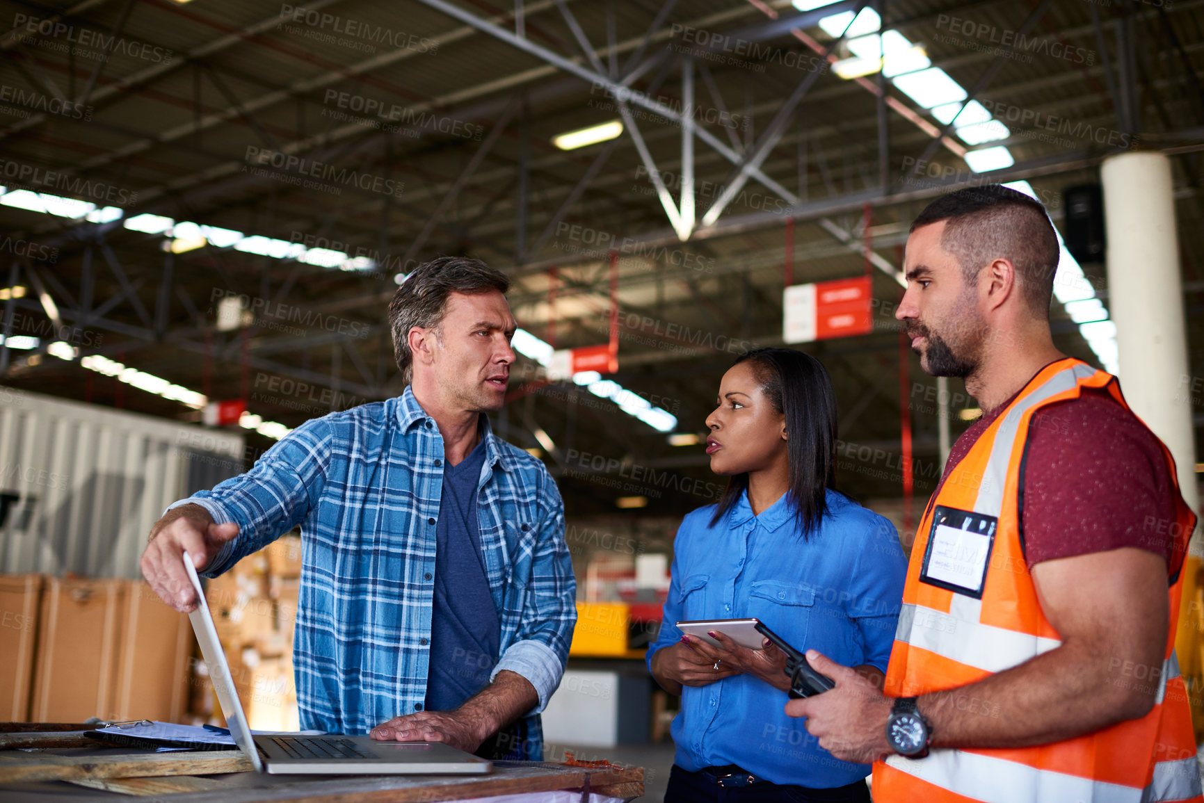 Buy stock photo Shot of a group of coworkers talking together over a laptop while standing in a large warehouse