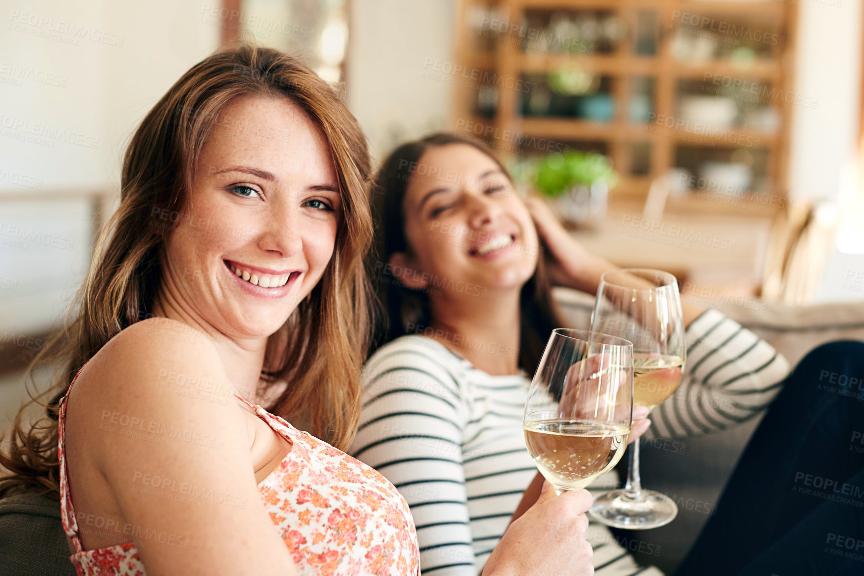 Buy stock photo Portrait of two young friends drinking wine while relaxing on the sofa