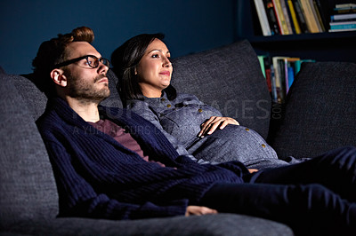 Buy stock photo Shot of a pregnant woman and her husband sitting on the sofa watching television in the evening