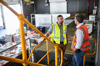 Buy stock photo Shot of two workers talking together while standing on stairs in a large warehouse