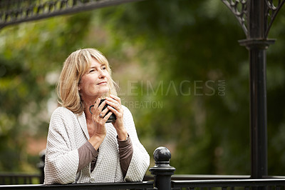 Buy stock photo Shot of a mature woman leaning against the railing of her front porch drinking a coffee