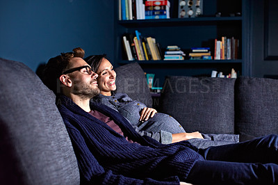 Buy stock photo Shot of a pregnant woman and her husband sitting on the sofa watching television in the evening