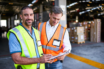 Buy stock photo Shot of two workers talking together over a clipboard inside of a warehouse
