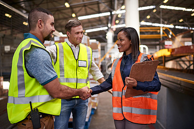 Buy stock photo Shot of two workers shaking hands together while standing in a large warehouse