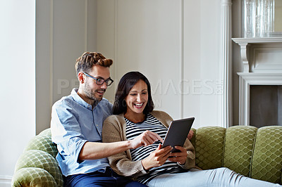 Buy stock photo Shot of a pregnant woman and her husband using a digital tablet while sitting on their sofa
