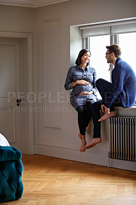 Buy stock photo Shot of a happy pregnant couple talking together while sitting on a window sill at home
