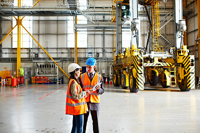 Buy stock photo Shot of two warehouse workers talking together over a digital tablet