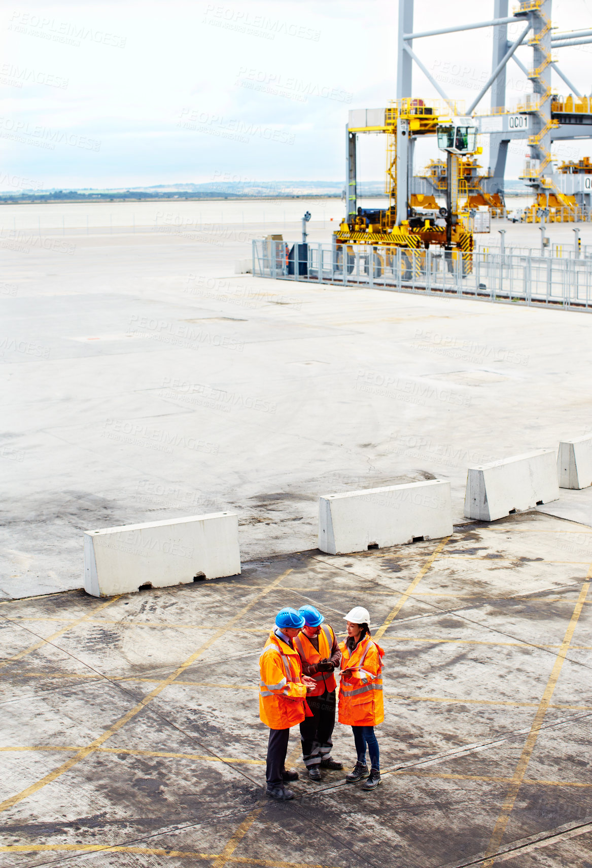 Buy stock photo High angle shot of three workers talking together while standing on a commercial dock