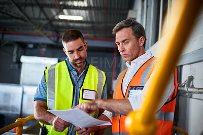 Buy stock photo Shot of two warehouse workers standing in a large warehouse discussing papework