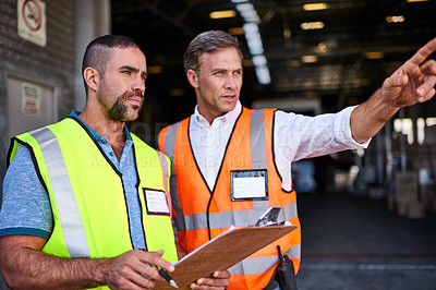Buy stock photo Shot of two workers talking together over a clipboard while standing at the entrance of a warehouse