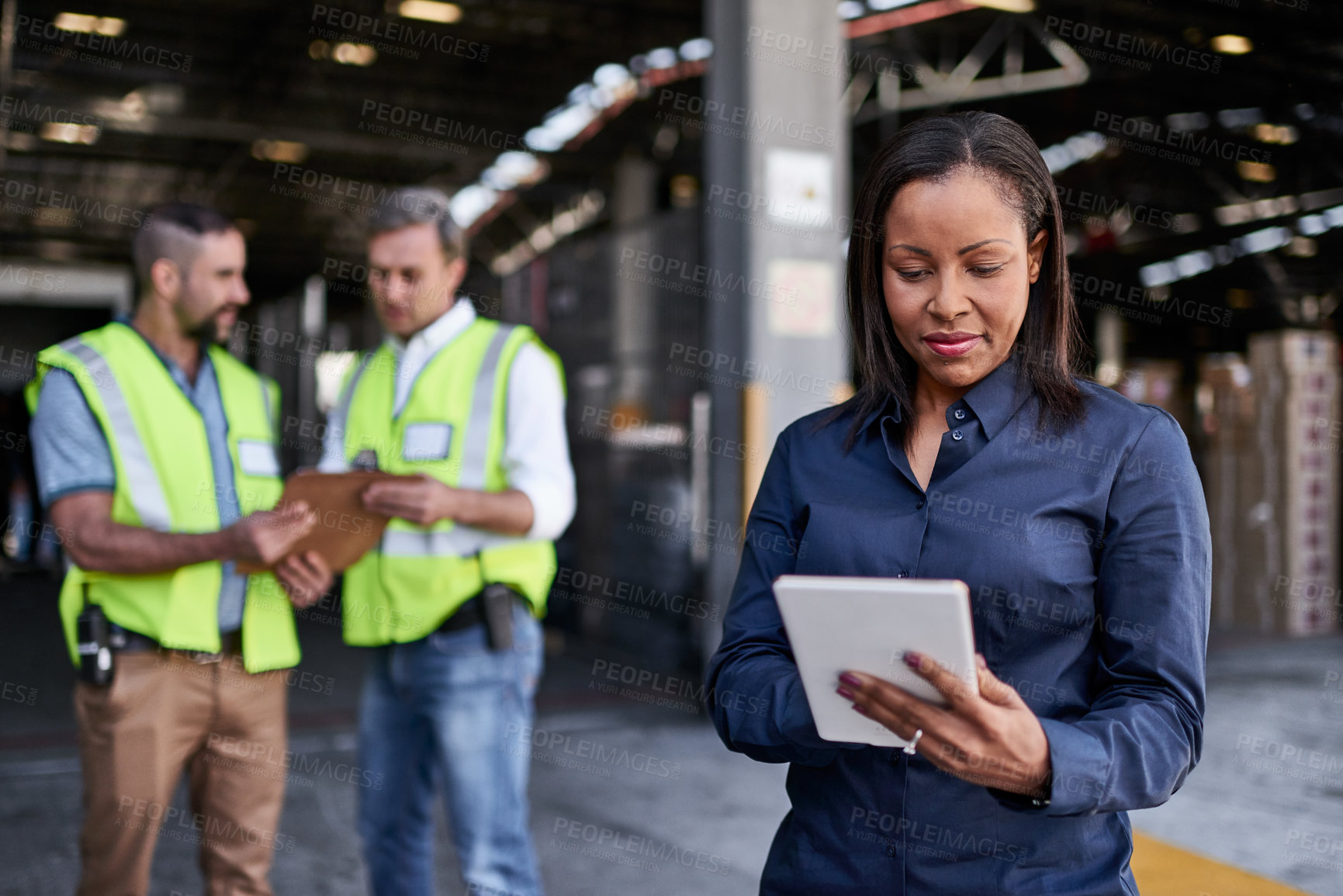 Buy stock photo Shot of a warehouse manager holding a digital tablet with workers in the background