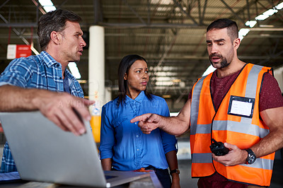Buy stock photo Shot of a group of coworkers talking together over a laptop while standing in a large warehouse