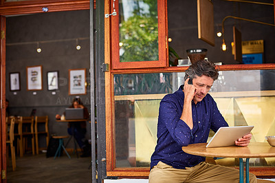 Buy stock photo Shot of a man talking on a cellphone and using a digital tablet while sitting in front of his cafe