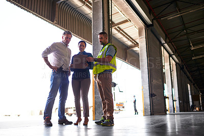 Buy stock photo Shot of three workers standing inside the entrance to a large warehouse