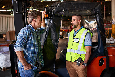 Buy stock photo Shot of two coworkers talking together by a florklift inside a large warehouse