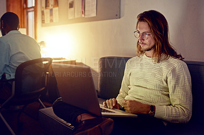 Buy stock photo Shot of a young man working on her computer in an office late in the evening