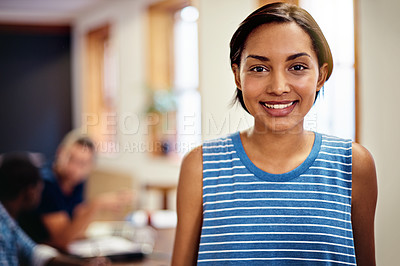 Buy stock photo Portrait of a smiling young woman standing in an office with colleagues working in the background
