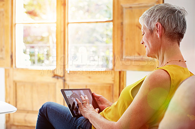 Buy stock photo Shot of a mature woman sitting in her living room using a digital tablet