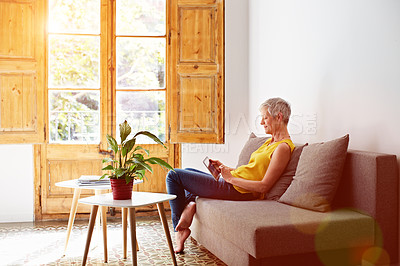 Buy stock photo Shot of a mature woman sitting in her living room using a digital tablet