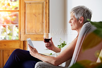 Buy stock photo Shot of a mature woman sitting in a chair at home relaxing with a digital tablet and a glass of wine
