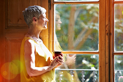 Buy stock photo Shot of a mature woman standing by a window at home drinking a cup of coffee