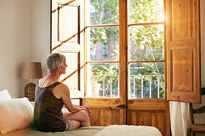 Buy stock photo Shot of a mature woman relaxing on a sofa by a window at home