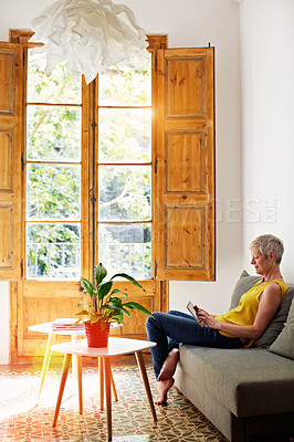 Buy stock photo Shot of a mature woman sitting in her living room using a digital tablet